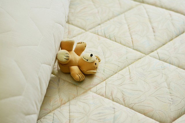 Odhrnutý paplón na matraci, na ktorom je plyšová medvedík.jpg